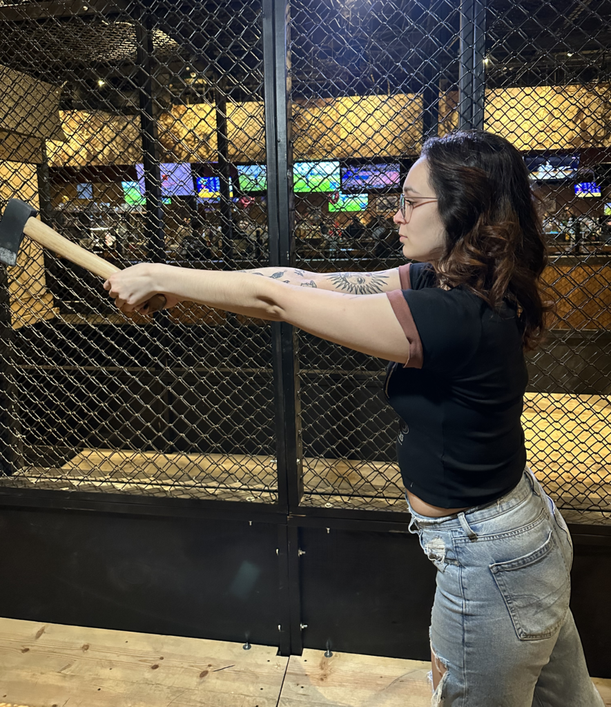 woman leaning forward and reaching out about to throw axe using two handed grip with eyes on target